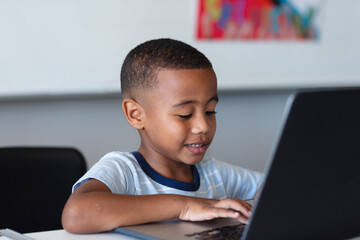 Smiling african american elementary schoolboy using laptop while sitting at desk in school