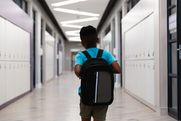 Rear view of african american elementary schoolboy with backpack walking in school corridor - Powered by Adobe