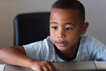 Close-up of african american elementary schoolboy using laptop while sitting at desk in school