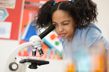 Biracial elementary schoolgirl looking through microscope during science practical class - Powered by Adobe
