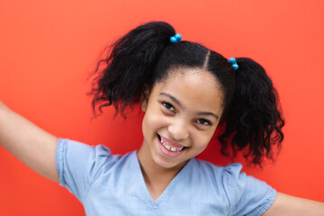 Portrait of smiling biracial elementary schoolgirl against orange background