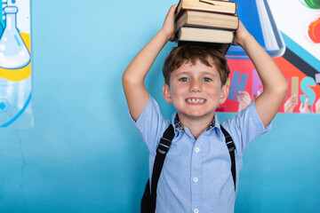 Portrait of smiling caucasian elementary schoolboy stacking books on head against wall in school