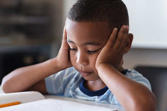 Close-up of african american elementary schoolboy reading book while sitting at desk in class