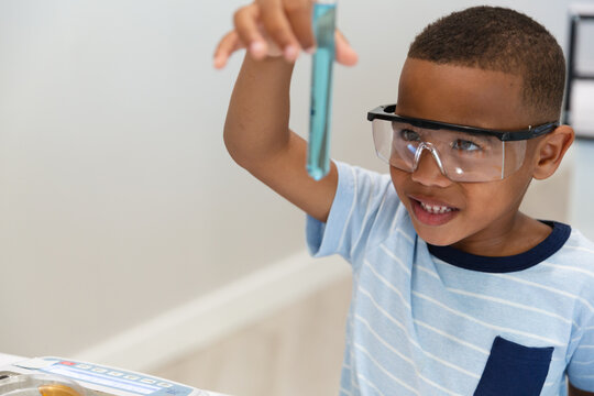 Smiling african american elementary boy looking at chemical in test tube while performing experiment