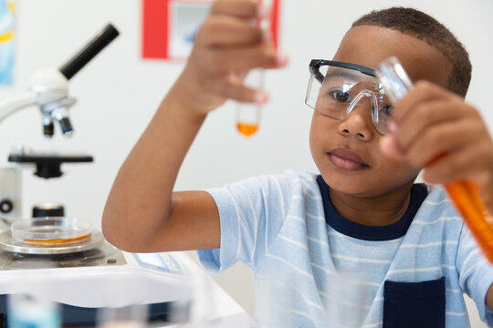 African american elementary boy looking at orange chemical in test tube during chemistry practical
