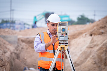 Surveyor engineer wearing safety uniform ,helmet and radio communication with equipment theodolite...