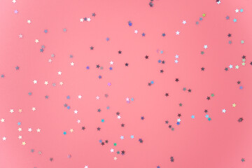 Silver stars glittering confetti on pink background. Trendy festive holiday backdrop. Many star-shaped particles for a postcard, invintation or web banner