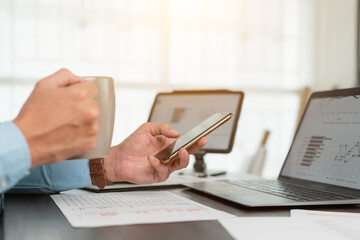 Close up business hand using smartphone and holding coffee cup while working at office.