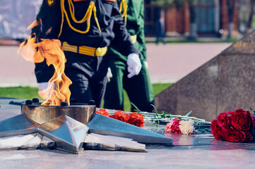 Eternal flame at the memorial to the unknown soldier. In the background, in blur, are men in full dress military uniform.