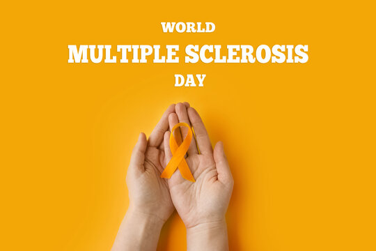 The woman's hands hold an orange ribbon on an orange background. Concept World Multiple Sclerosis day. Leukemia cancer awareness. COPD and ADHD.