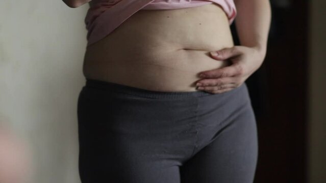 overweight, a woman in the mirror looks at her fat belly