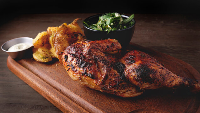 Peruvian food, Pollo a la brasa or grilled half chicken with fried yellow potatoes and arugula salad, wooden board. Selective focus