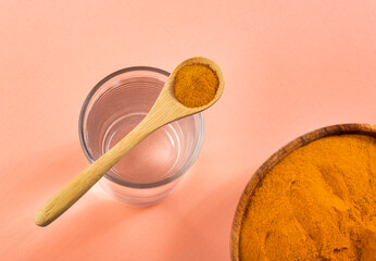 Spoon with organic turmeric and glass of filtered water - Curcuma longa