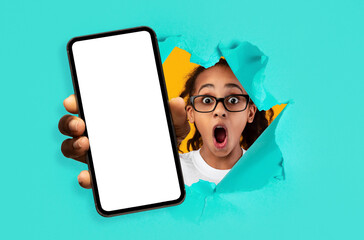 Shocked girl showing white empty smartphone screen breaking through paper