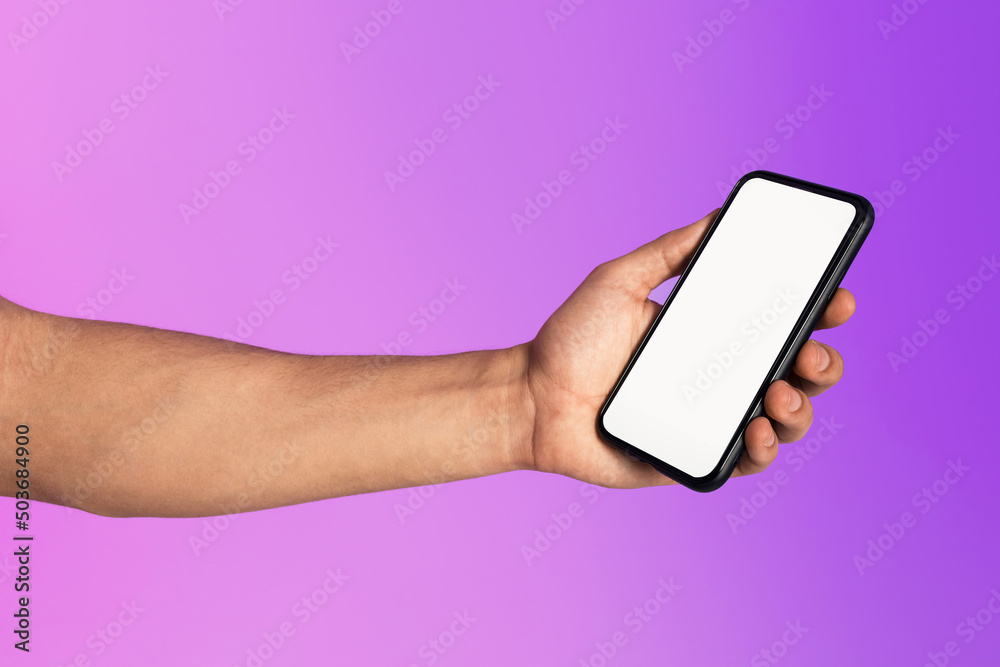 Poster cropped view of millennial man holding cellphone with empty white screen in neon light, mockup for m