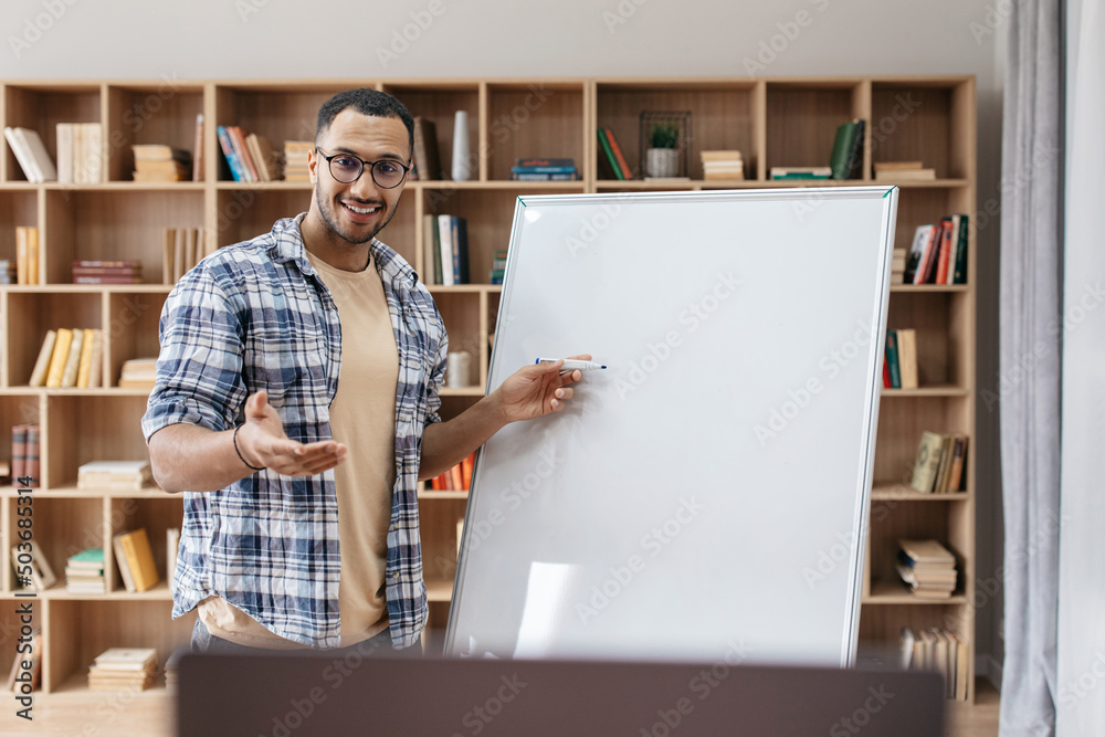 Poster Presentation concept. Portrait of happy male manager standing near blank empty whiteboard and pointing at copy space