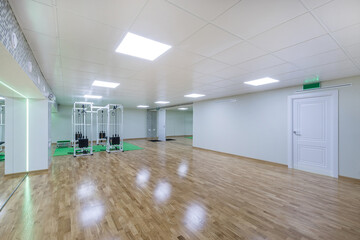A large, bright gym with brown laminate flooring, an entrance door and sports equipment.