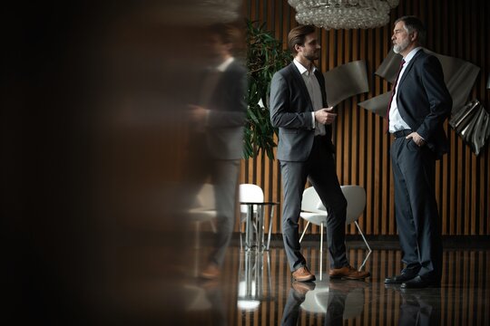 Two businessmen deep in discussion together while standing in modern office.