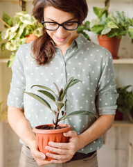 Smiling Beautiful female gardener in glasses take pot with plant and look dawn