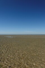 Wet North Sea beach at low tide under a blue spring sky (vertical), Sahlenburg, Lower Saxony, Germany