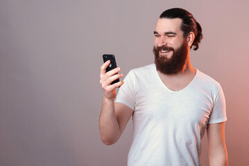 Handsome bearded man is looking on a phone while smiling wide.