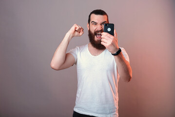 Powerful bearded man is making the winner gesture while holding a phone.