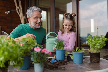 Little daughter helping father to plant and water flowers, home gardening concept