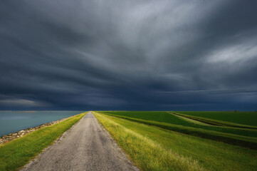 Strada rurale con campi di erba verde e cielo con temporale e nuvole in arrivo - 503690579
