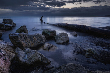 Alba o tramonto lungo la costa, con scogli e tronchi nel mare con acqua con effetto seta - 503690599