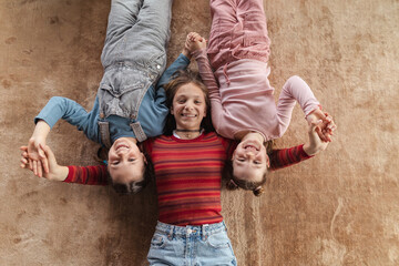 Top view of happy three sisters kids lying on floor and looking at camera.
