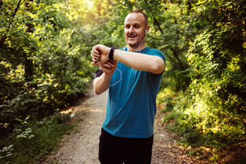 Young Caucasian men using Smart Watch measuring heart rate during walk. Runner fixing time at sports smart watch. Young athletic man using fitness tracker or smart watch before run training outdoors.