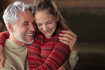 Portrait of teenage daughter hugging her happy father at home.