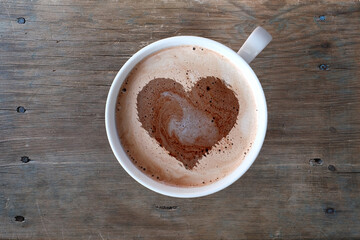 close-up of white cup with coffee cappuccino on an old brown wooden table, foam in form of silhouette of human heart, concept of mind, caffeine addiction, top view, copy space for designer