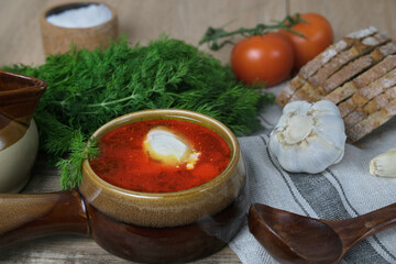 hot soup in plate on rustic table, red borscht with beets, vegetables, red tomatoes, bread, garlic, dill greens, concept of cooking Ukrainian traditional food, cuisine of peoples of world