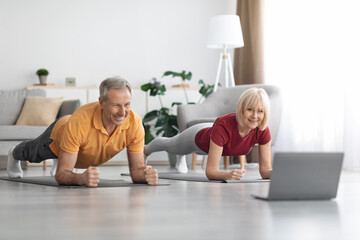 Athletic senior man and woman training at home, using notebook