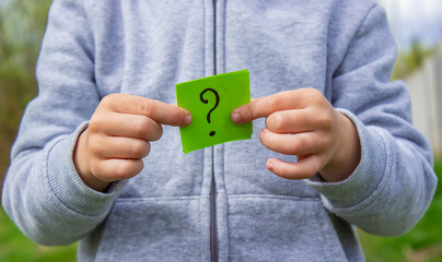the boy holds stickers with a question mark on the background of the park. Nature.
