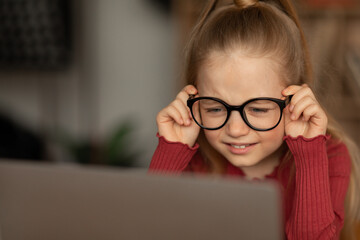 Little Girl Squinting Eyes Using Laptop Wearing Glasses At Home