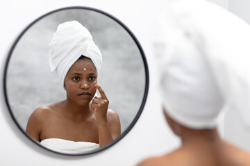 Reflection of african american mid adult woman in towel applying moisturizer on face
