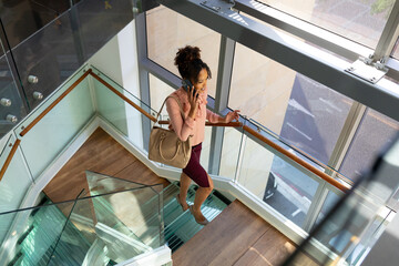 African american mid adult businesswoman with purse talking on phone while climbing steps in office