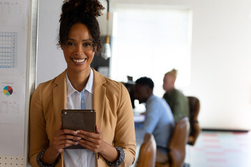 Portrait of smiling african american mid adult businesswoman with digital tablet standing in office