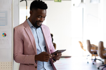 Smiling african american mid adult businessman using digital tablet while standing in office