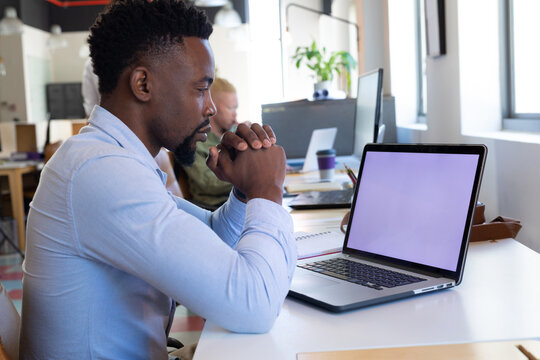 African American Mid Adult Businessman With Hands Clasped Looking At Laptop With Blank Screen