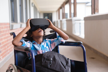 African american elementary schoolboy wearing vr glasses while sitting on wheelchair in corridor