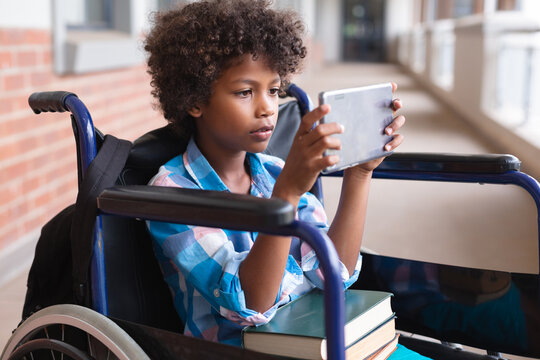 African american elementary schoolboy using digital tablet while sitting on wheelchair in corridor