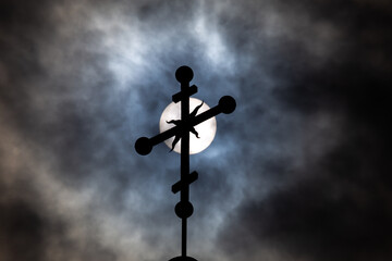 Orthodox cross on top of the church against the dramatic sky. Photo taken against the sun behind the clouds.
