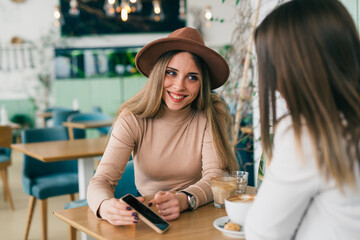 women friends using mobile phone on coffee break in cafeteria