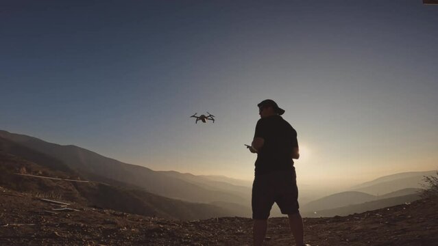 Drone pilot takes off device from his hand to work on photographs, topography and videos. Mountain top at sunset.