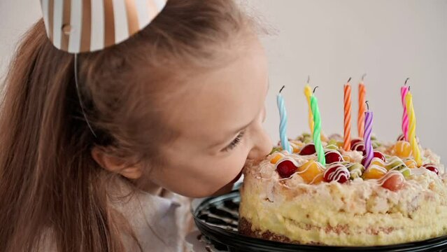 A happy child bites a big cake at a table on a light background. A funny little girl eats a delicious a dessert.