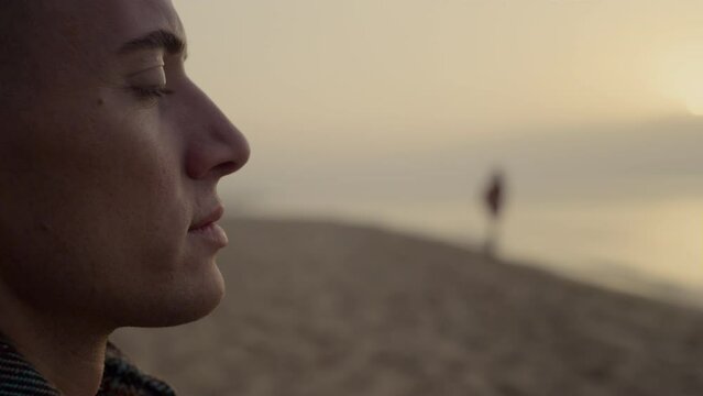 Thoughtful man enjoying ocean landscape at sunset. Dreamy guy blinking eyes
