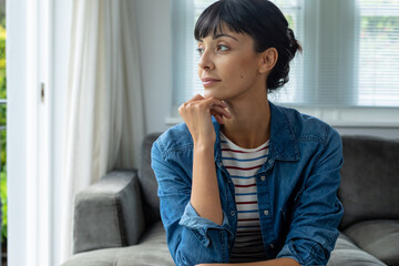 Contemplative caucasian young woman sitting with hand on chin at home